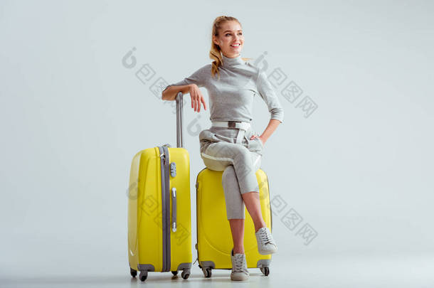 美丽的微笑的女人<strong>坐在行李箱上</strong>交叉的腿在灰色的背景, 旅行概念