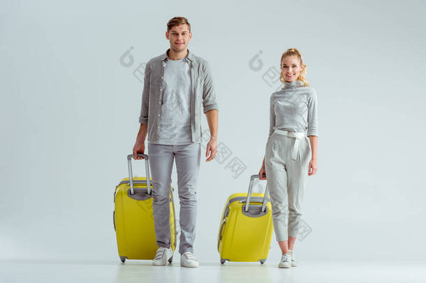 带着黄色行李箱的微笑夫妇, 看着灰色背景的相机, 旅行概念