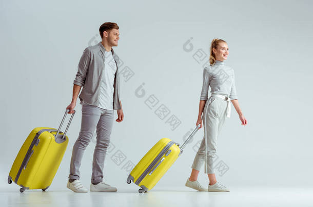 微笑的夫妇携带黄色行李箱灰色背景, 旅行概念