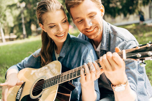 特写镜头的年轻微笑的女人学习弹吉他与男朋友在公园