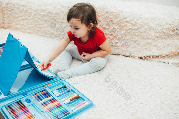 一个穿着红色T恤的小女孩正在画一个带有红色记号的蓝色画架