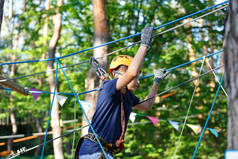 快乐, 可爱, 穿着蓝色 t恤和头盔的年轻男孩, 在冒险公园玩, 拿着绳子, 爬上木梯。积极的生活方式概念