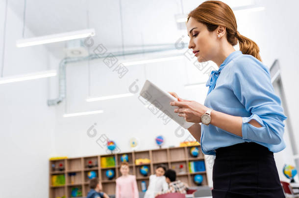 认真的老师在蓝色上衣使用数字平板电脑在课堂上