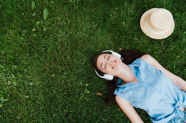 高高兴兴的女人躺在草地上，在草帽旁听着音乐 