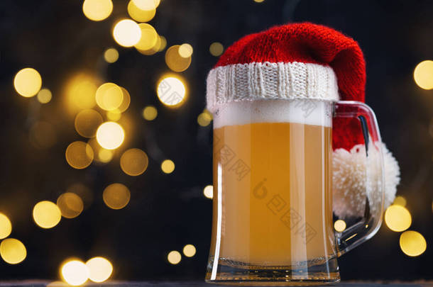 圣诞啤酒啤酒杯在圣诞老人的帽子黑暗的背景与bokeh花环。手工艺啤酒