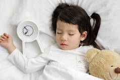 小女孩和泰迪熊睡在卧室的木床上，快乐的亚洲小女孩和闹钟早上醒来
