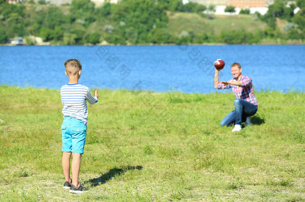 愉快的父亲和儿子在河附近演奏橄榄球