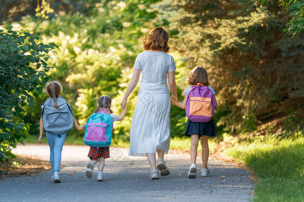 父母和小学生是紧密联系在一起的.背着背包的女人和女孩开始上课。秋天的第一天.