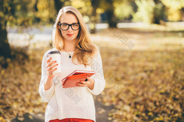 年轻金发女学生<strong>戴眼镜</strong>, 长头发捧着咖啡, 在公园户外看书秋季时间教育, 生活方式和人的概念.