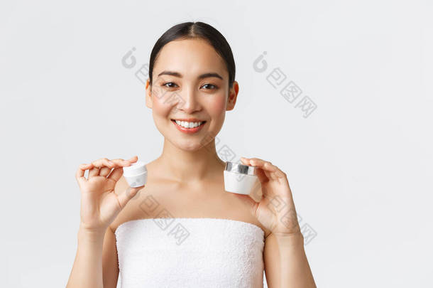 美容美发、个人<strong>护理</strong>、温泉沙龙及护肤理念.漂亮的亚洲女人穿着浴巾，脸上有两种乳霜和眼霜，笑着推荐使用水合作用，滋养<strong>肌肤护理</strong>疗法