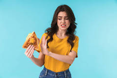 照片上年轻美丽的女子举着三明治站在蓝色墙壁上，显得很不高兴，她举手投足.