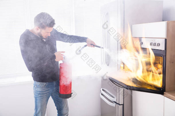 年轻人用红色灭火器阻止厨房里的炉子着火