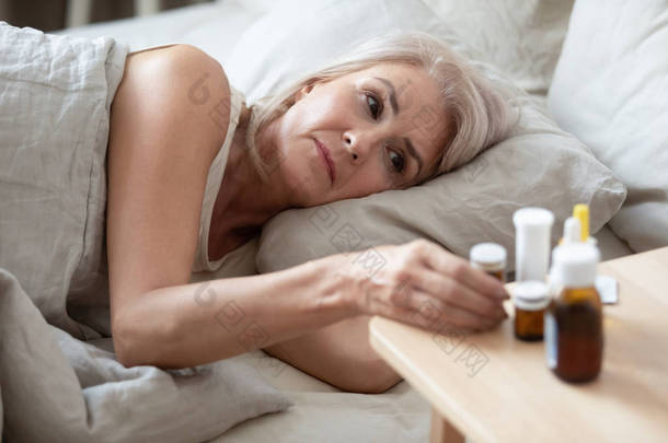 不健康的老年妇女从床头柜吃药特写