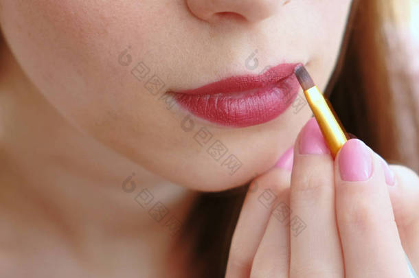 特写的女人的手与刷子, 把明亮的口红在她的嘴唇上.
