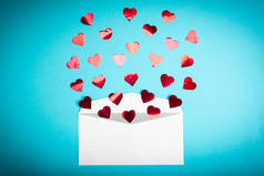 红色的五彩纸屑心在浅蓝色的背景下从白色的信封里飞出。情人节。爱的概念送给爱人的礼物