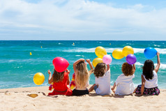 坐在海滩上彩色的气球上的儿童.