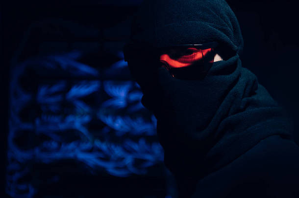 眼睛和面具下的黑客在背景下看摄像头的模糊视图