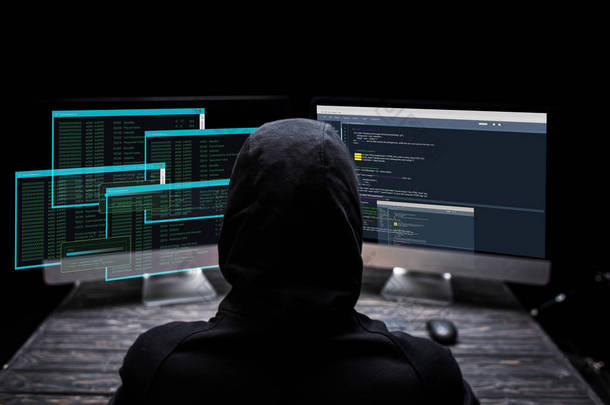 黑屏上有数据的头罩黑客坐在计算机监视器旁边的背景图 