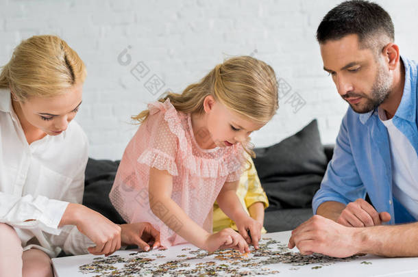 父母与可爱的小女儿玩拼图片在家里