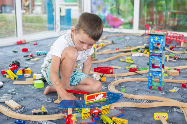 小孩子在地板上玩木制铁路。小男孩玩木火车集