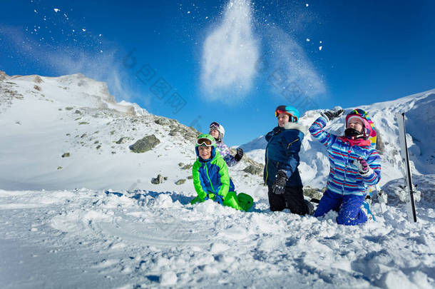 一群孩子一起坐在地上玩乐，在美丽的山上向空中扔雪