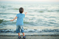 海边的小男孩在日落时把石头扔进水里。快乐的童年.