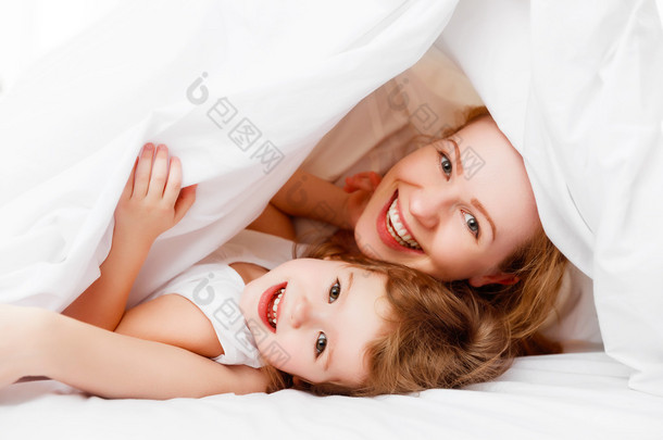 快乐家庭的母亲和孩子玩、 笑着躺在床上 