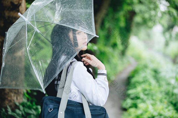 在雨中漫步在自然人行道上的亚洲学校女孩肖像