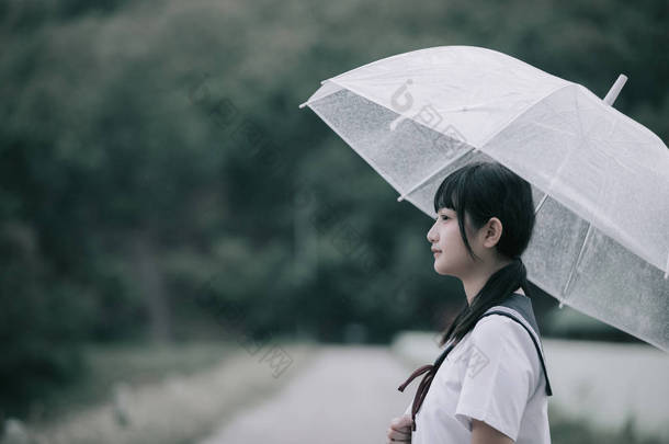 在雨中漫步在自然人行道上的亚洲学校女孩肖像