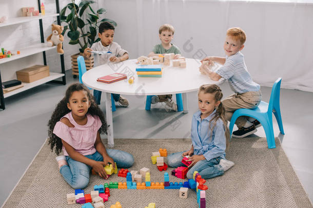 多种族学龄前儿童在课堂上玩木块时看相机