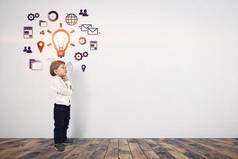 可爱的小男孩在黑色牛仔裤和衬衫的想法站在一个灰色的墙壁与商业图标和灯泡。商业神童和他的想法概念。模拟