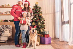 家庭和女儿在圣诞老人帽子与狗在鹿角摆在圣诞树与礼品盒在家里