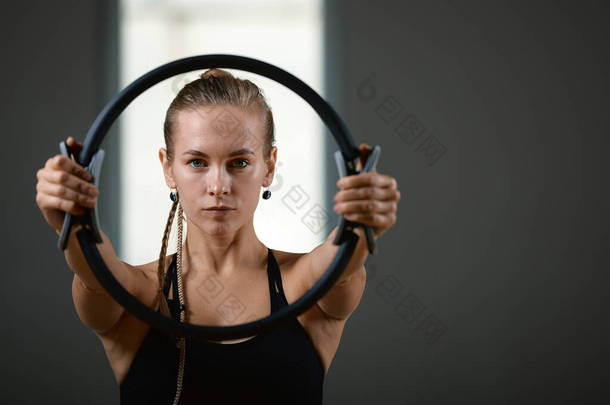 年轻的，漂亮的，运动的女孩正在做运动与普拉提环在健身房灰色背景。 穿着蓝色绿色西服的斯拉夫女运动员 复制<strong>空间</strong>，灰色背景，体育<strong>横幅</strong>为