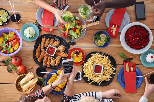 坐在木制餐桌前和一群人一起吃饭的头像。食物在桌子上。人们吃快餐.