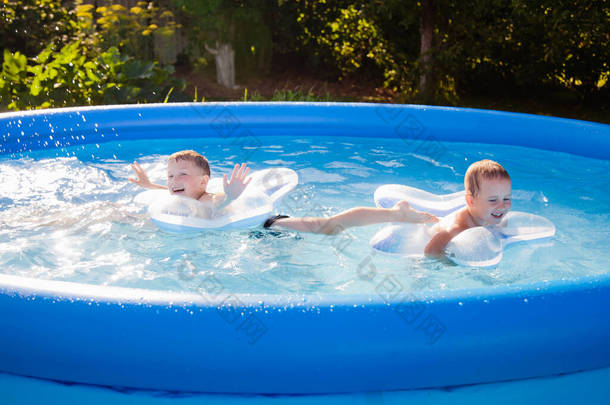 两个男孩在游泳池里快乐地游泳，在充气的圆圈上，形似一颗星星。夏天和水上娱乐活动的概念.