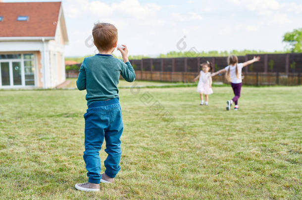 后视图肖像的小男孩玩的绿色草坪上的朋友在院子里享受夏日户外