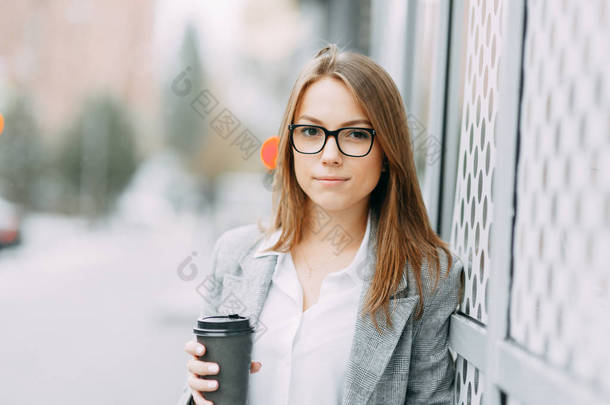 女孩博主与咖啡站在街上, 等着开会。时尚和微笑的女孩。一个快乐的买主, 一个现代的咖啡店.