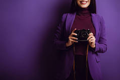 拍照时，微笑的摄影师拿着紫色背景的数码相机