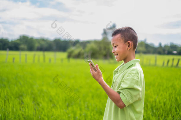 亚洲男人的肖像亚洲男人的小孩站在那里玩智能手机。在线学习不仅仅是在课堂上学习。他在稻田里吃着绿米，夕阳西下.