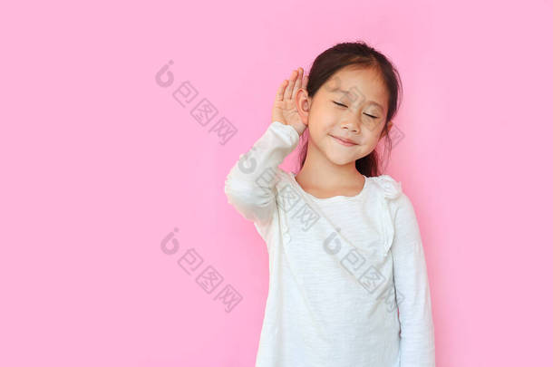 闭上你的眼睛亚洲小女孩一边<strong>微笑</strong>一边用手捂住耳朵一边听谣言或流言蜚语在粉色孤立的背景下带有复制空间.