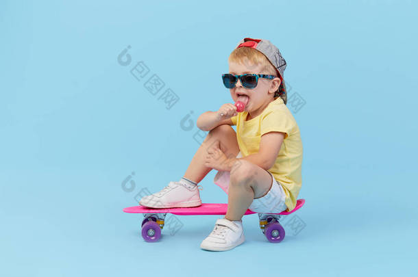 时尚<strong>幼儿</strong>男孩在眼镜与滑板有乐趣的<strong>蓝色背景</strong>