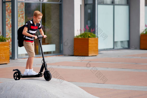 <strong>上学</strong>的男孩骑着他的电动滑板车在城里带着背包在阳光明媚的日子里。穿五颜六色衣服的孩子在<strong>上学</strong>的路上骑车