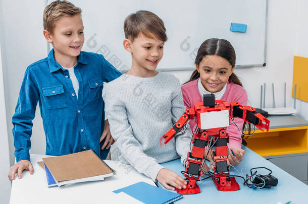 快乐的学童在茎类的办公桌上触摸红色手工机器人