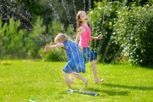 阳光明媚的夏日, 可爱的小女孩在后院里玩洒水车。可爱的孩子们在<strong>户外</strong>享受水的乐趣。有趣的夏季游戏为孩子们.