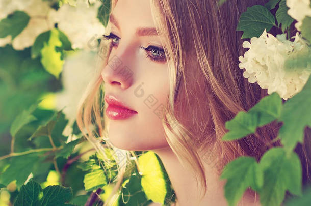 美丽的春天女孩在芬芳的白花在夏天开花公园。女人在一个盛开的花园。时尚, <strong>化妆品</strong>和香水。卷发金发