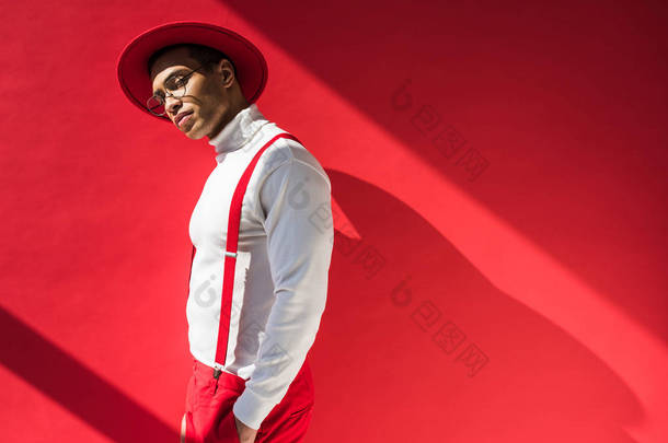 时尚的混血男子在帽子和吊带摆在红色与复制空间