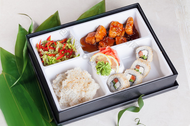 寿司商务午餐盒里，三文鱼烧滚芝麻、 大米、 芥末、 腌的姜顶上，竹叶孤立、 白色背景