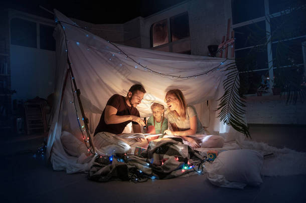 一家人坐在帐篷里，用手电筒讲故事