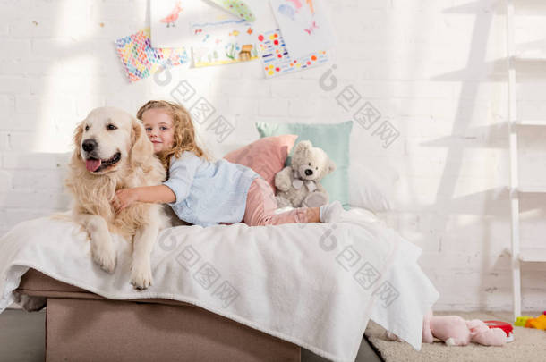 可爱的孩子抱着可爱的金毛猎犬在床上在儿童房