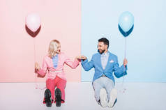 笑着的女人和英俊的男人，戴着气球，在粉色和蓝色的背景上摆出拳头对拳头的姿势 
